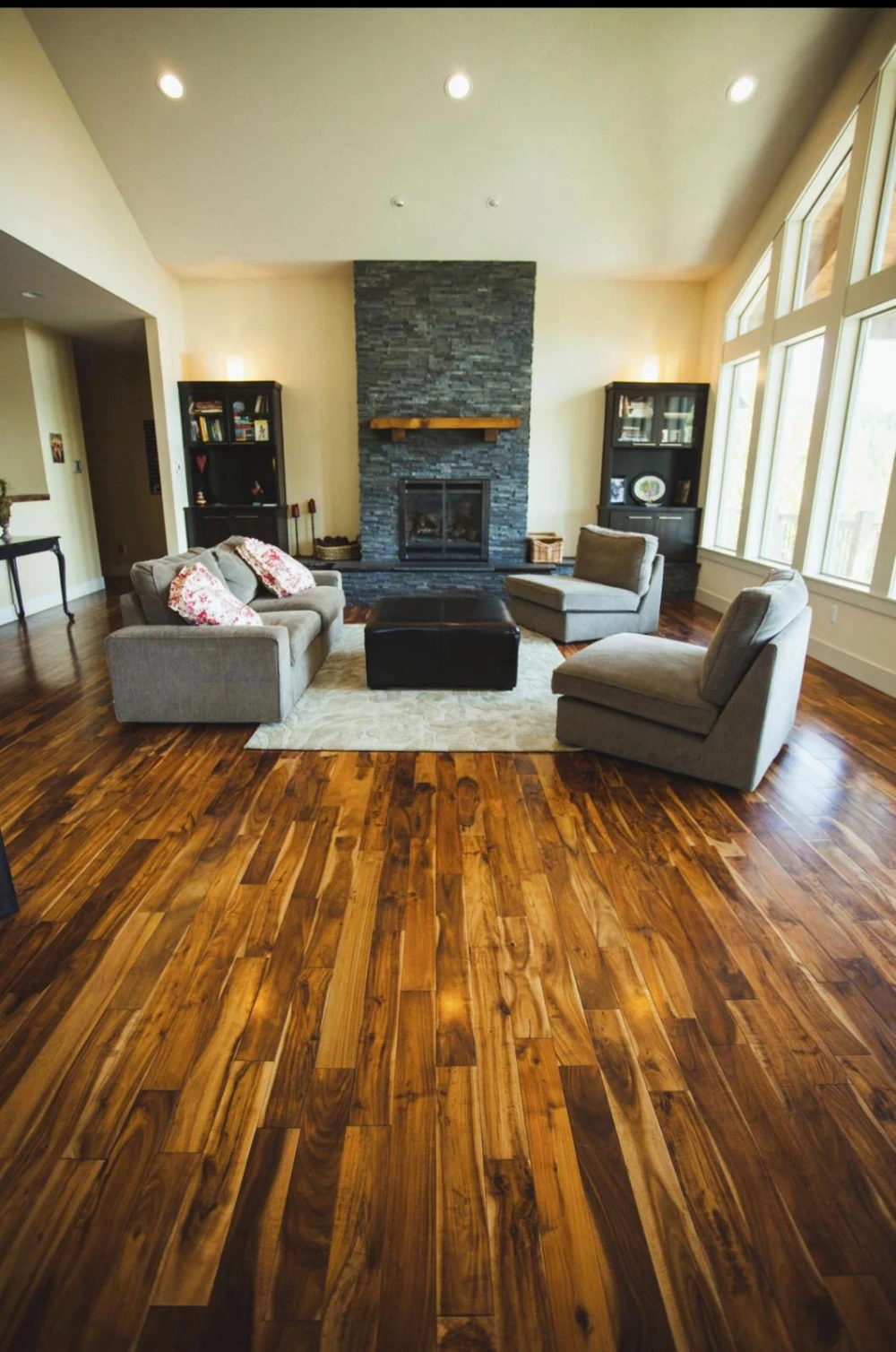 Warm tongue-and-groove hardwood floor in a living room with stone fireplace
