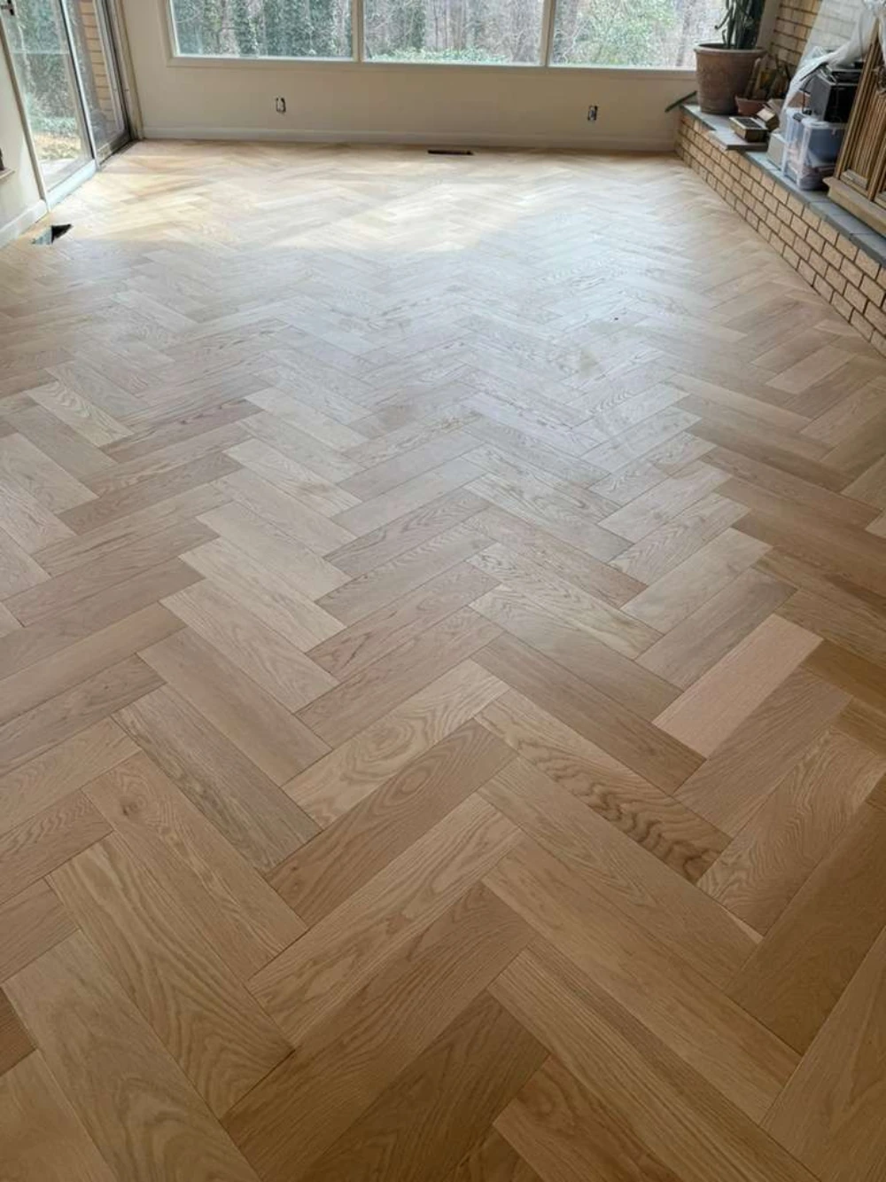 Light white-oak herringbone floor in a living room with brick fireplace