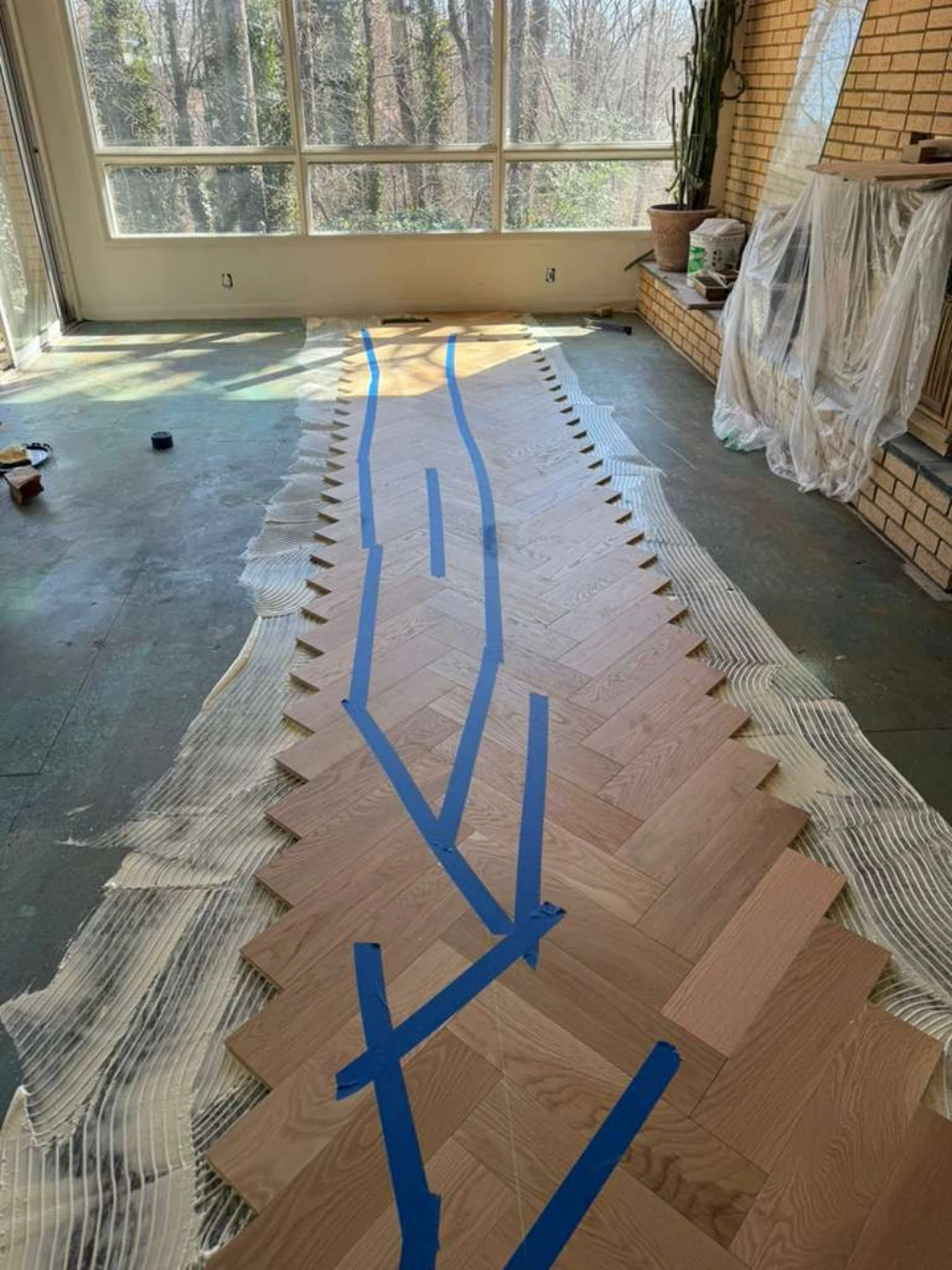 Herringbone hardwood floor installation in progress in a window-lined room